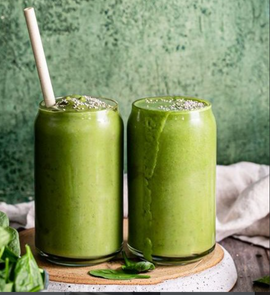 Two green smoothies in glasses with a straw on a wooden board against a green background.